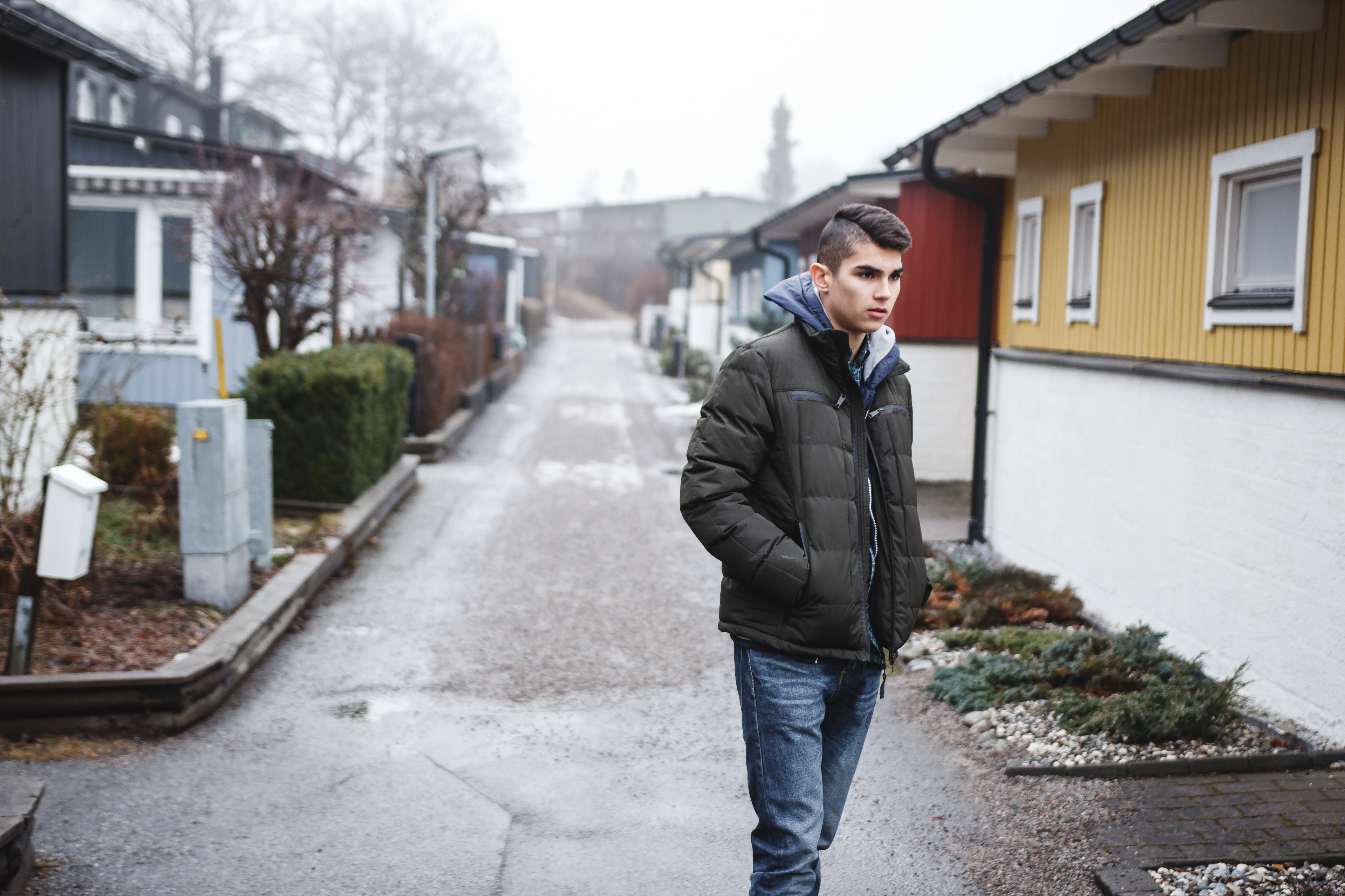 En tonårskille i dunjacka på en gata i ett villaområde 