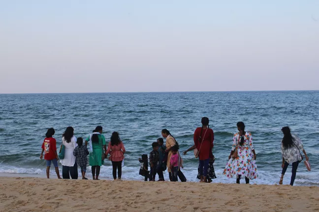 People facing the water at the beach by sunset 