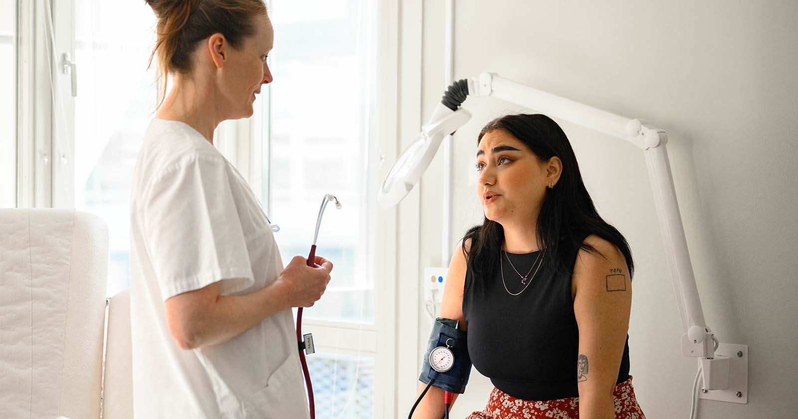 En barnmorska pratar med en patient som sitter på en brits, foto. 