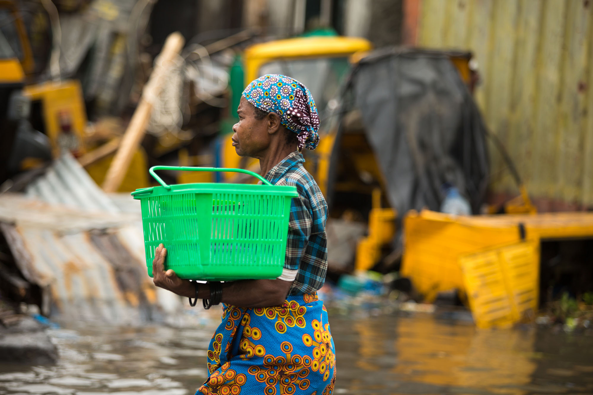 Woman walking in a flooded environment, carrying a green plastic basket. 