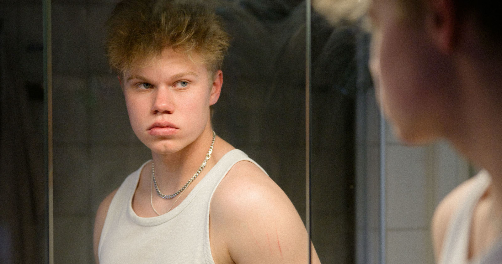 En blond kille ser sig själv i ett badrumsspegel, lite arg eller missnöjd. 