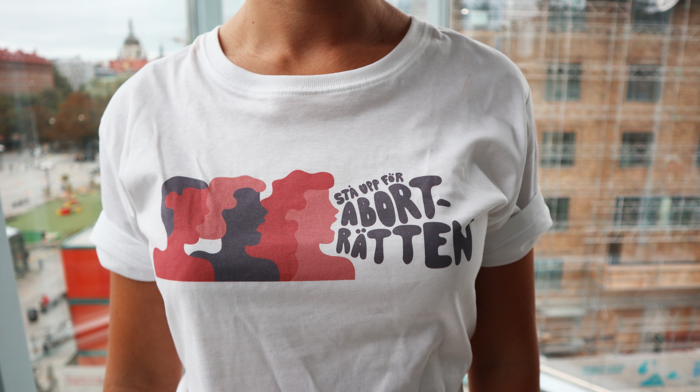 En person har på sig en vit t-shirt med en illustration av tre personer och texten "Stå upp för aborträtten". 