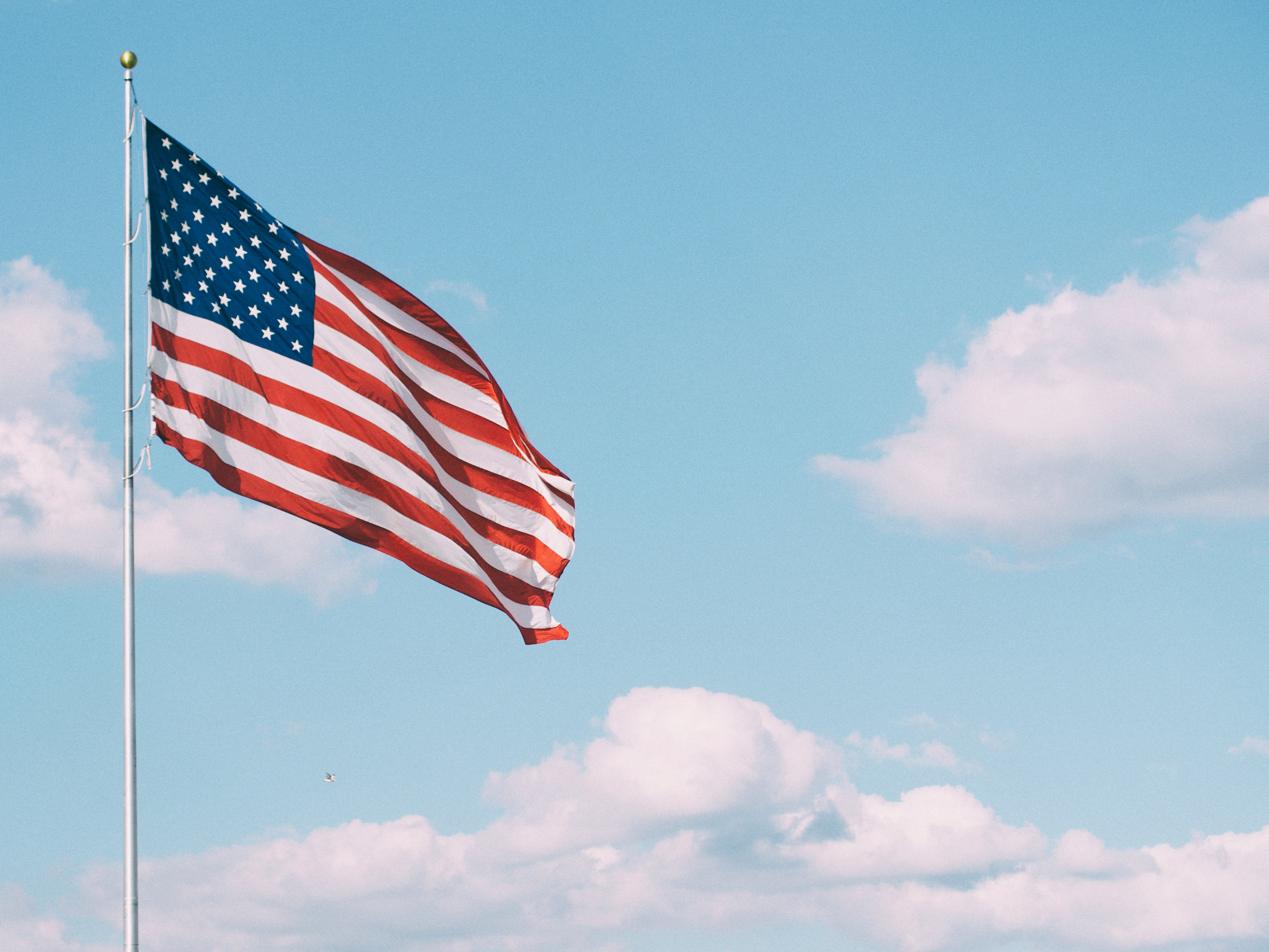 Den amerikanska flaggan vajar mot blå himmel och moln, foto. 