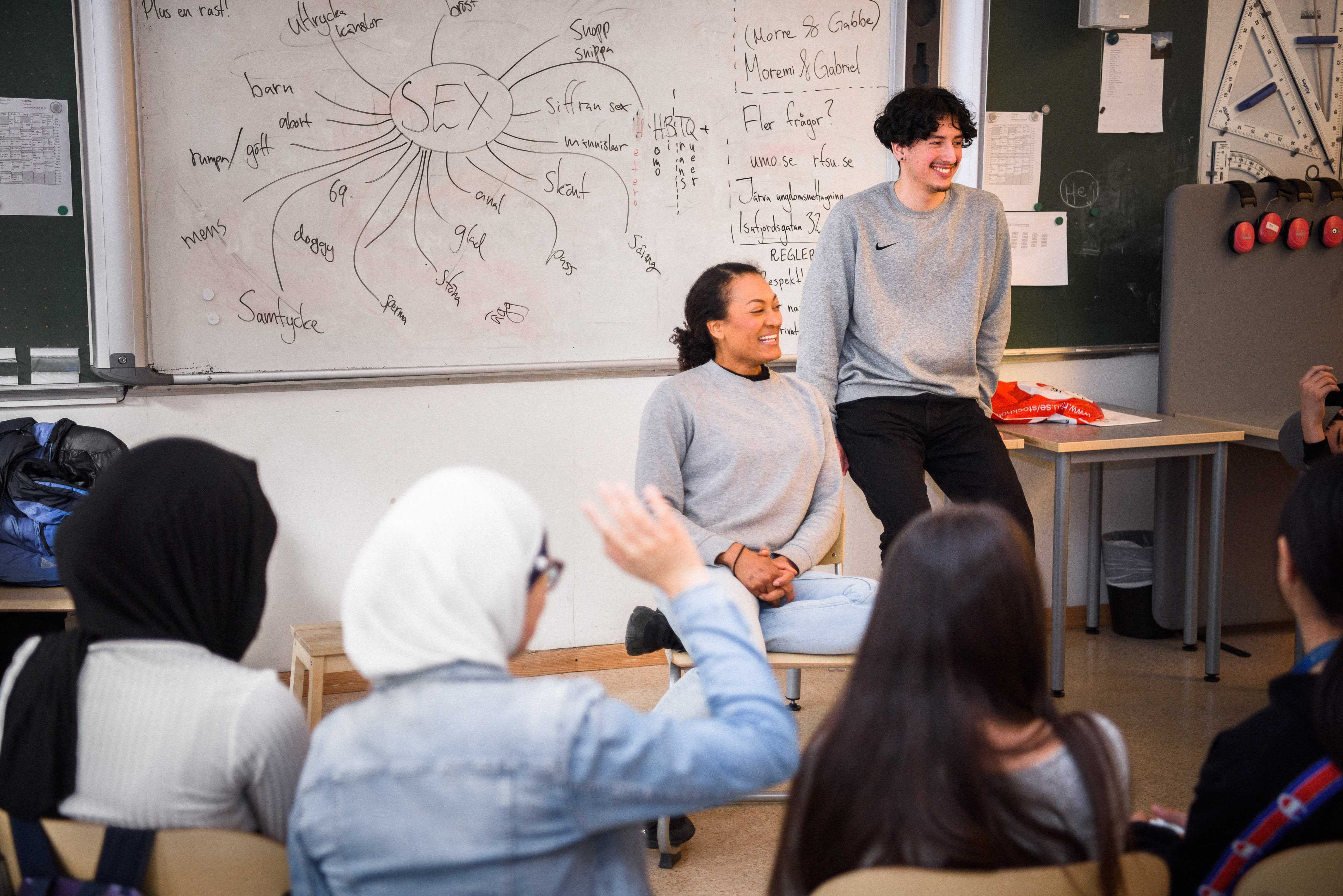 Två av RFSU:s sexualupplysare ler och tittar ut mot en skolklass. 