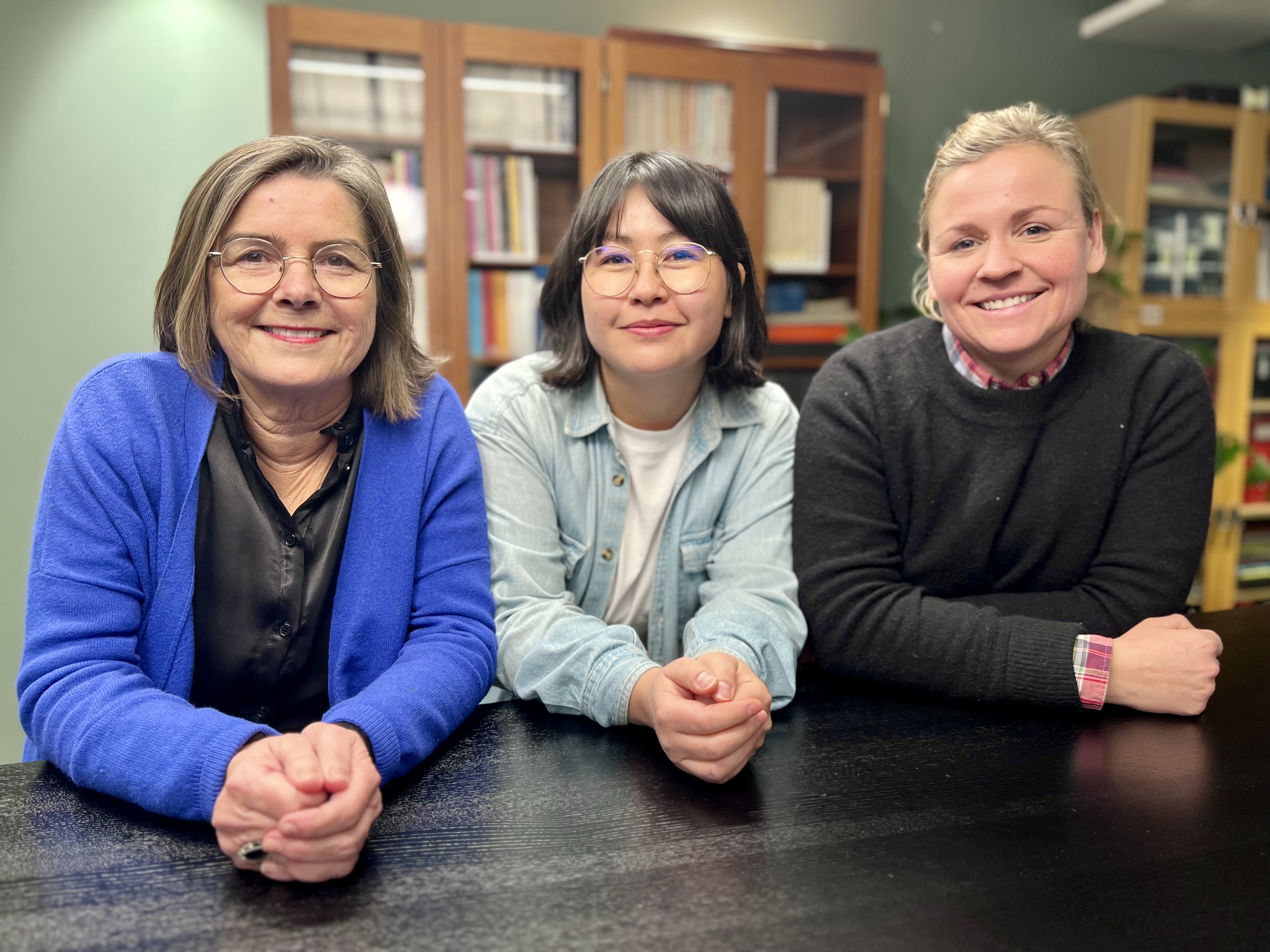 Ingela Holmertz, Hana Suzuki Ernström och Karin Olsson står bredvid varandra och lutar sig mot ett bord.  