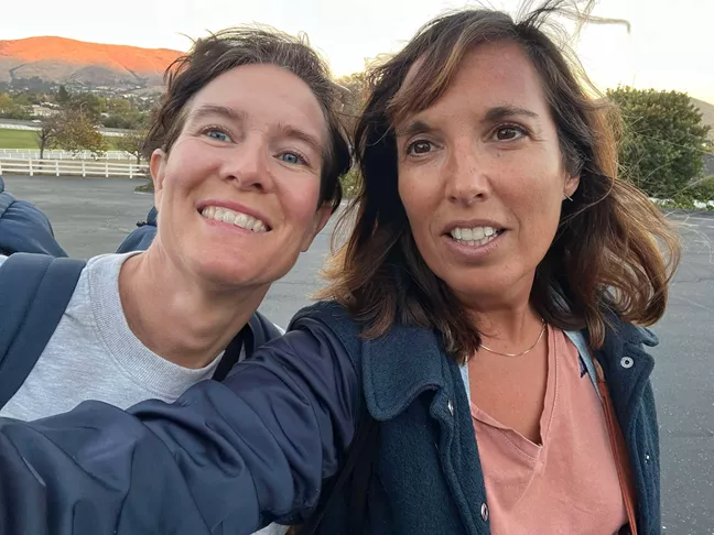 Två personer tar en selfie tillsammans. Ett stort berg syns i bakgrunden. 