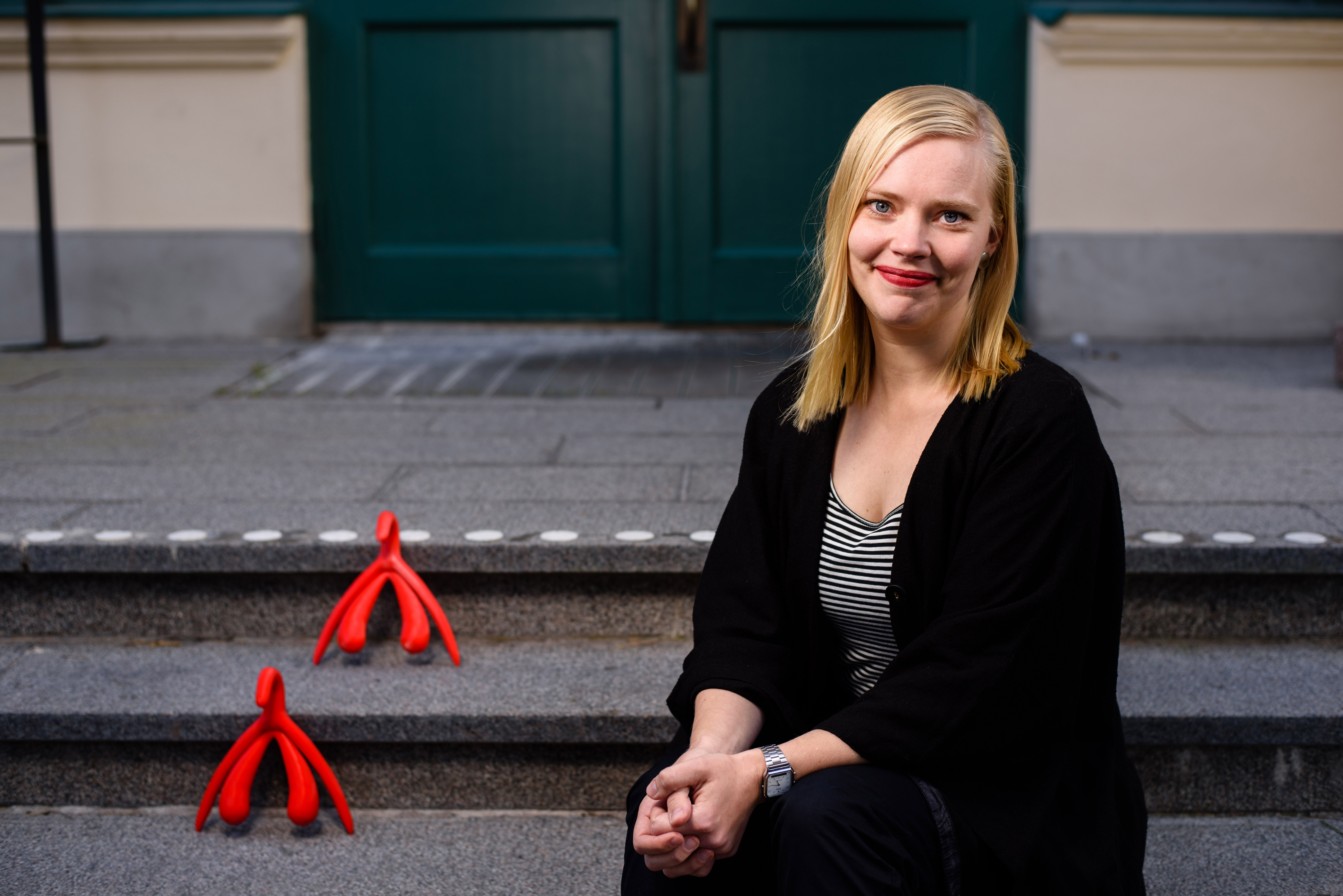 Jessica Påfs sitter på en trappa bredvid två klitorisfigurer i plast. 