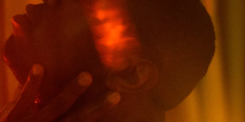 Man i profil för sin hand mot örat. Rummet är fyllt av orangeaktigt ljus.  