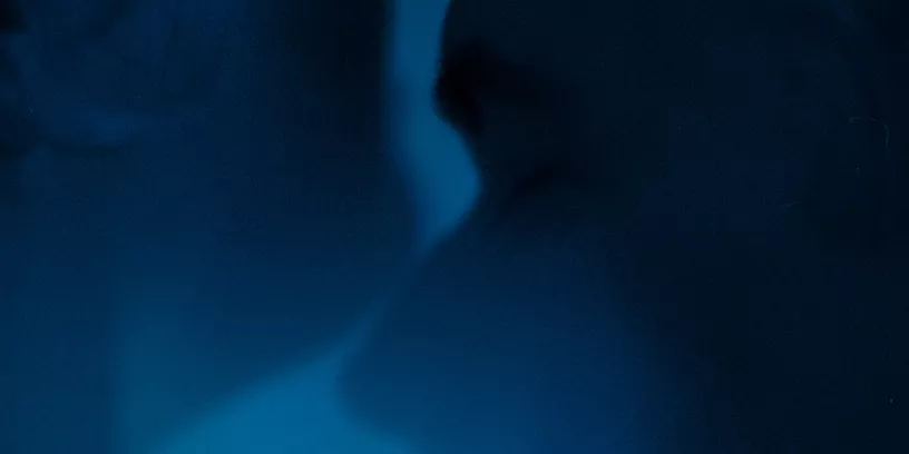Två ansikten vänd mot varandra i profil. Det är blått ljus i rummet. 